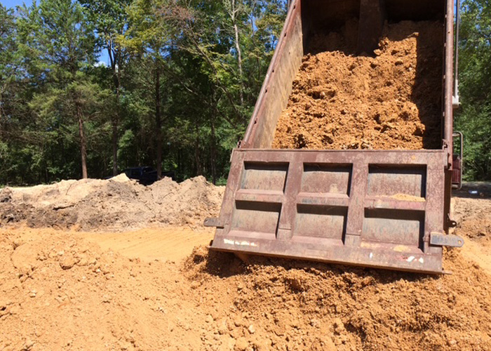 Dump truck unloading a pile of orange dirt
